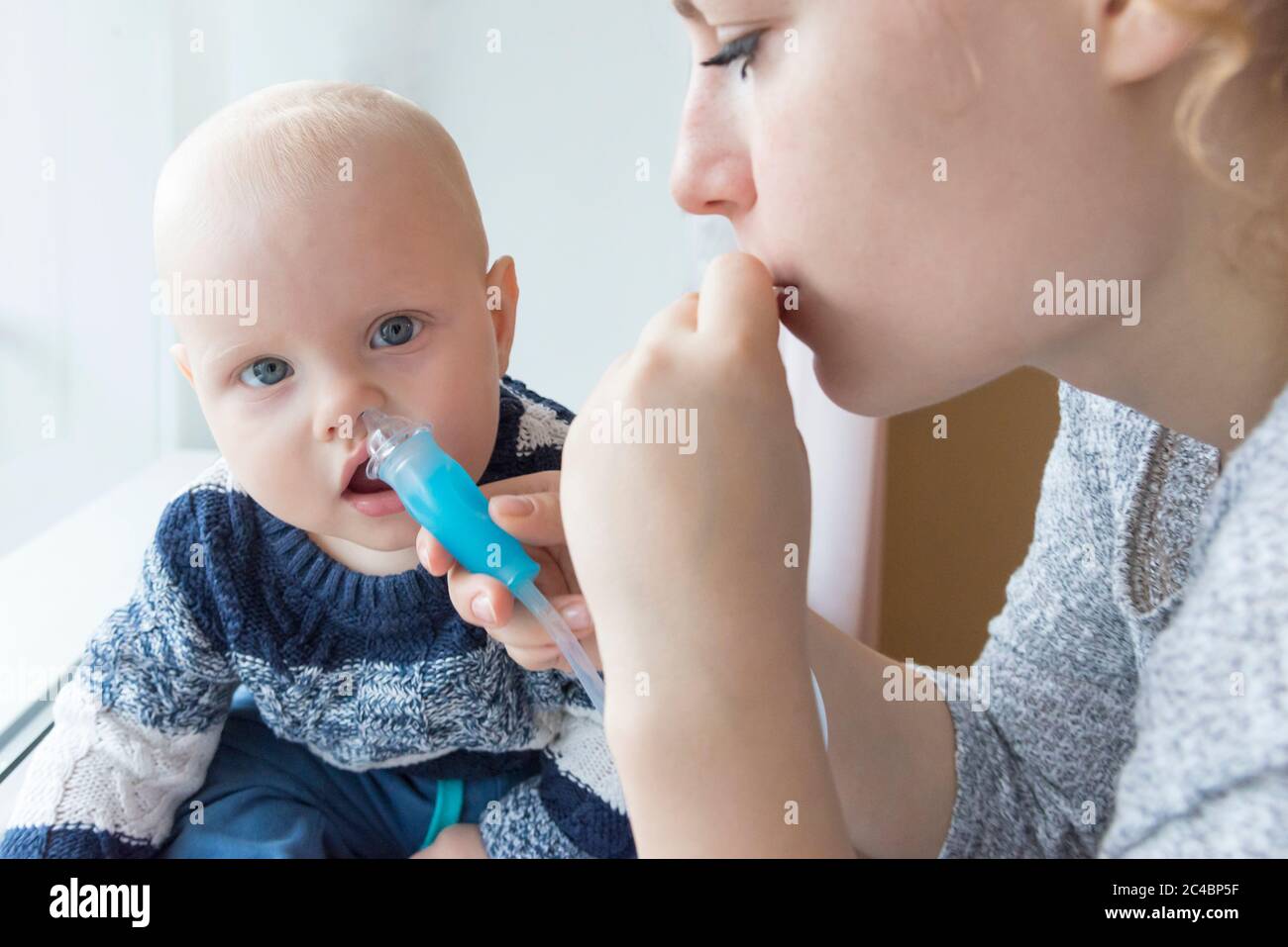 Mom cleans baby's nose from mucus using a nasal aspirator Stock Photo