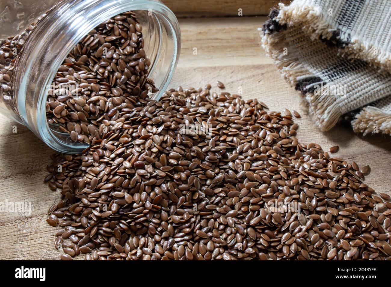 Flax seed falling from glass jar on rustic table. Flaxseed is an organic and healthy grain packed with natural nutrients often used in a vegetarian di Stock Photo