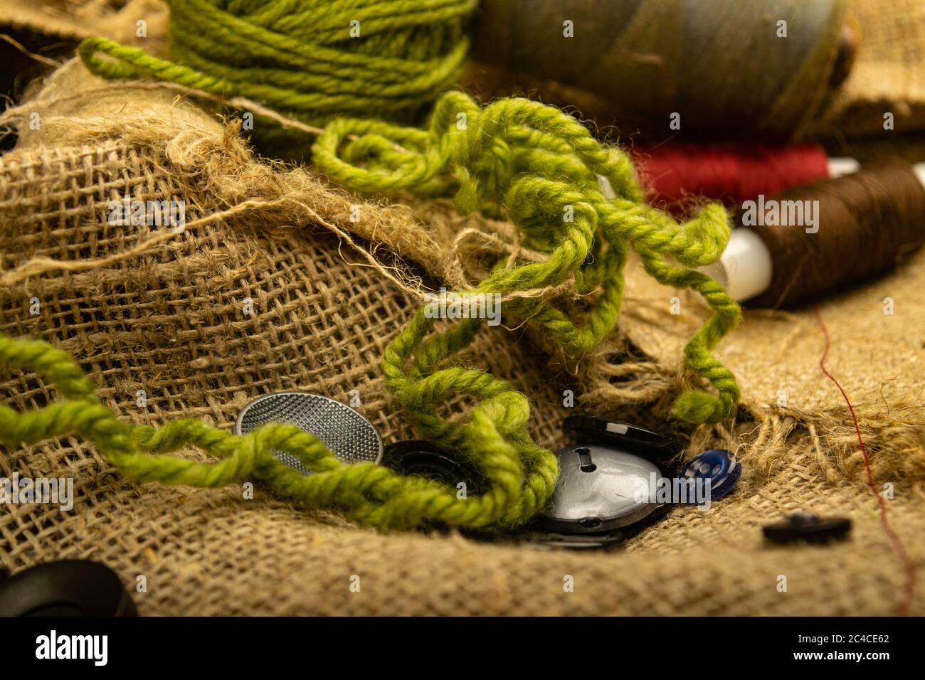 Various buttons and multicolored threads on coarse-textured burlap. Close up Stock Photo