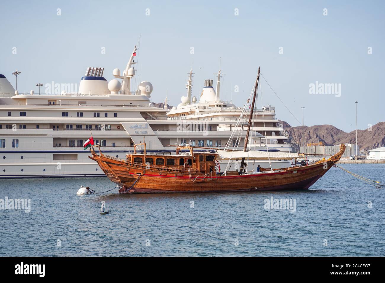 Muscat / Oman - February 15, 2020: traditional historic wooden boat next to  large tourist cruise ship anchored in the port of Muscat Stock Photo - Alamy