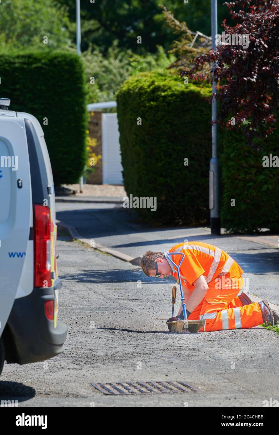 Anglian Water operative, in bright fluorescent suit, at work on a street to mend leaks and inspect drains. Stock Photo