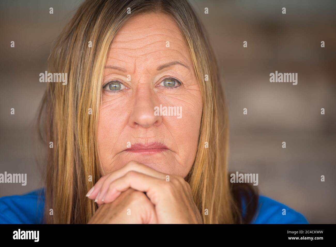 Portrait attractive mature woman with worried, thoughtful facial expression, chin on hands, blurred background. Stock Photo