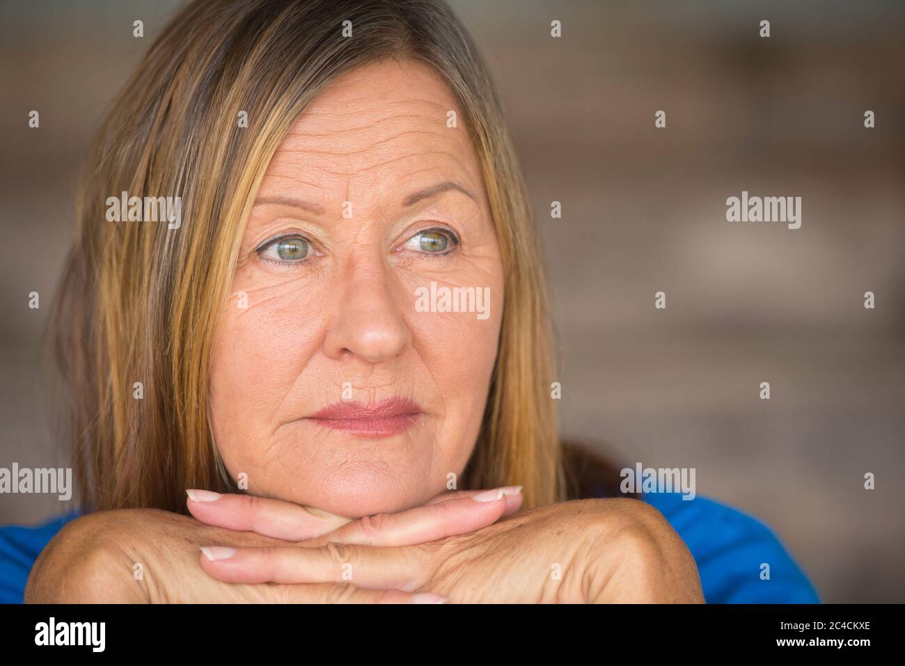 Portrait attractive mature woman with relaxed confident, thoughtful facial expression, chin on hands, blurred background. Stock Photo