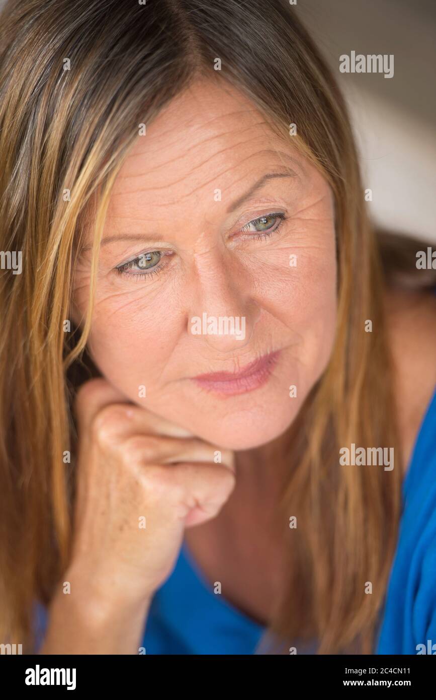 Portrait attractive mature woman with thoughtful lonely facial expression, relaxed, peaceful daydreaming, blurred background. Stock Photo