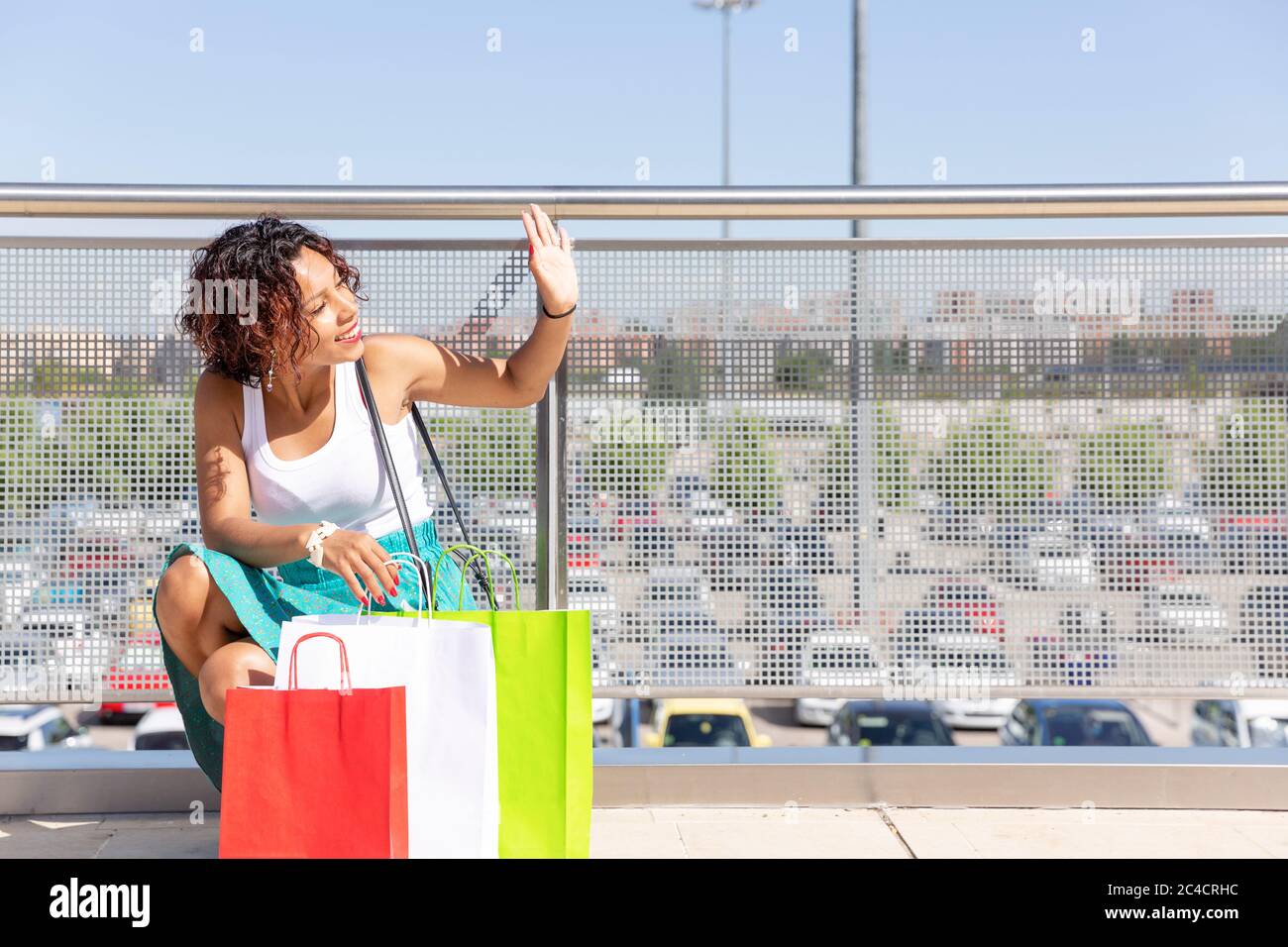 Young woman with exotic features greets with her hand at the entrance of a shopping center. Space for text. Stock Photo