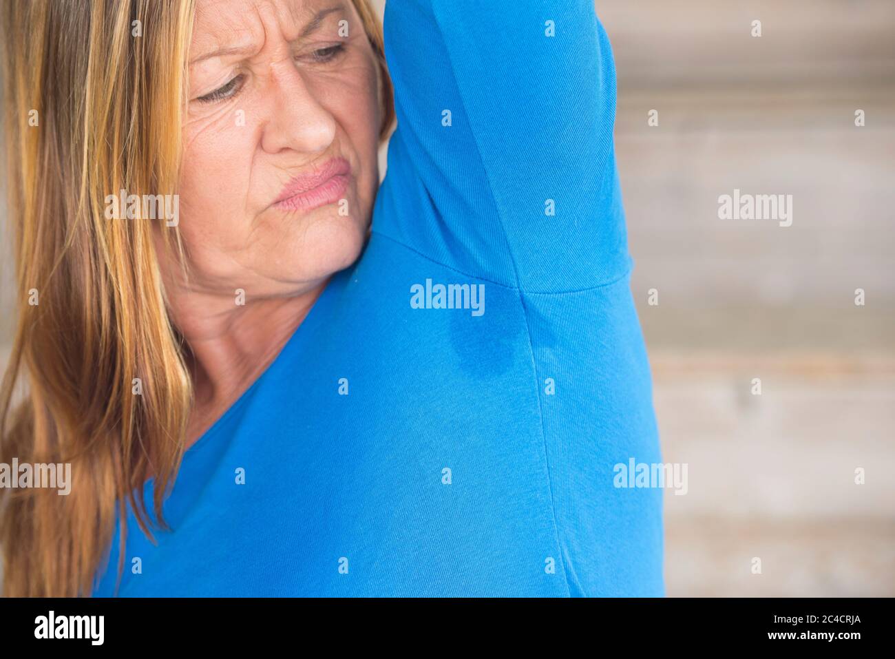 Portrait angry mature woman with smelly sweat perspiration under arm with  wet moisture spot on blue shirt, blurred background, copy space Stock Photo  - Alamy