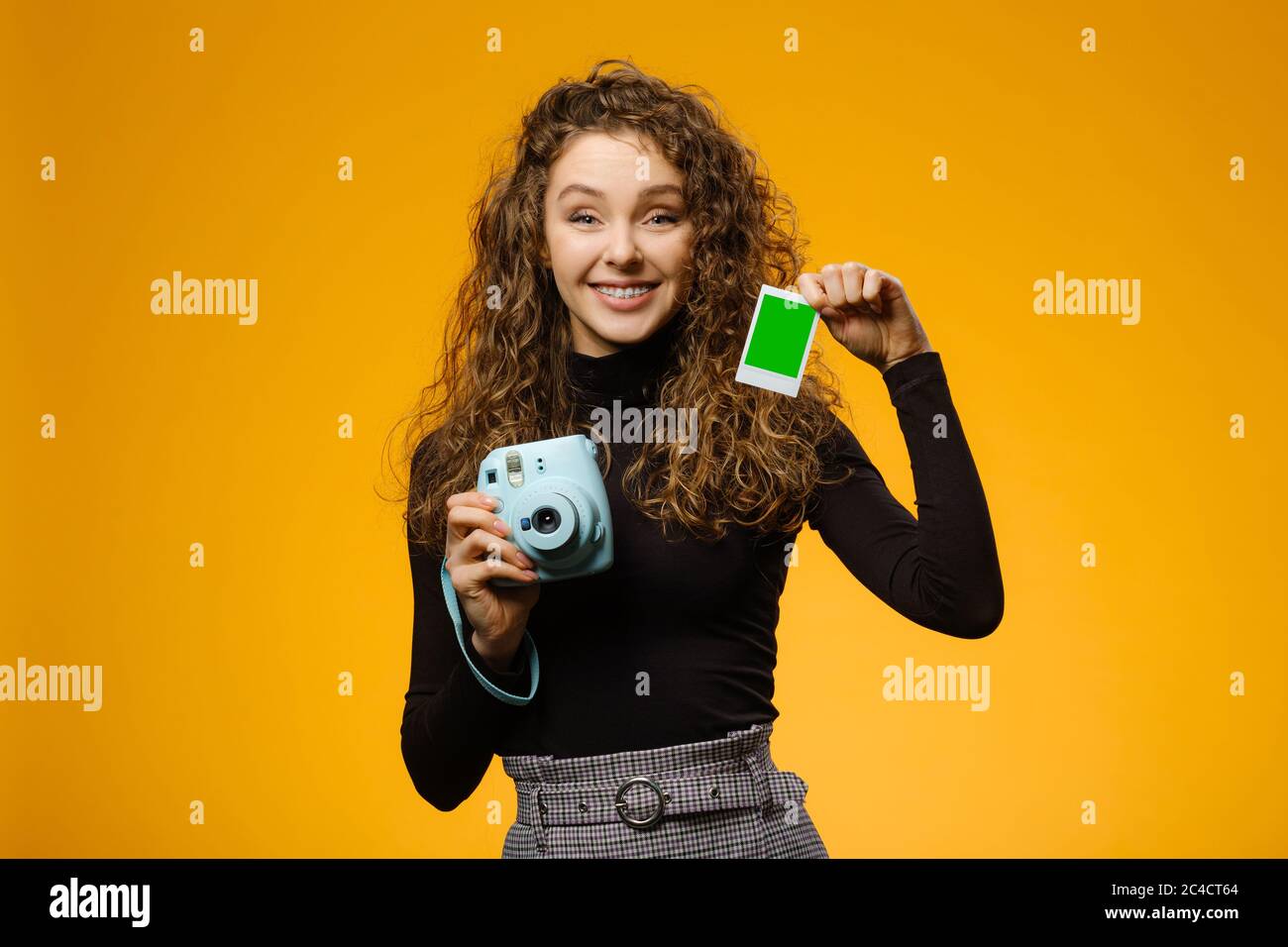 Happy girl with instant film camera isolated on yellow background. Model is holding blank frame with mockup space on a picture Stock Photo