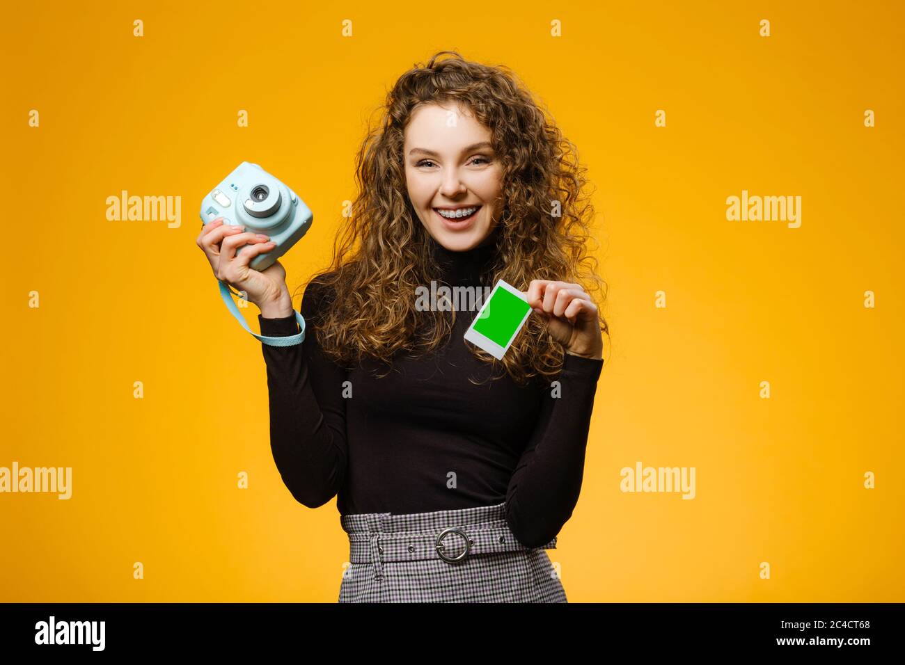 Beautiful girl with instant film camera isolated on yellow background. Model is holding blank frame with mockup space on a picture Stock Photo