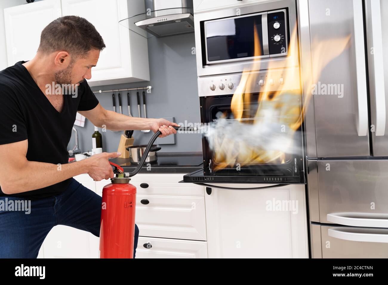 Man Using Fire Extinguisher To Put Out Fire From Oven At Home Stock Photo -  Alamy