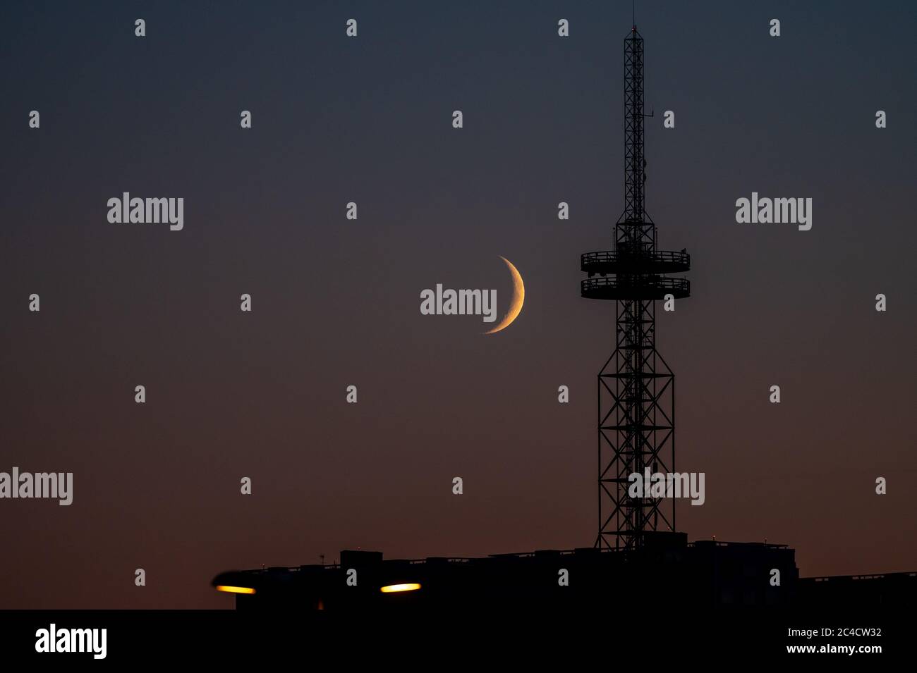 A silhouette of a radio broadcast mast against the cloudless sky and the moon. Stock Photo