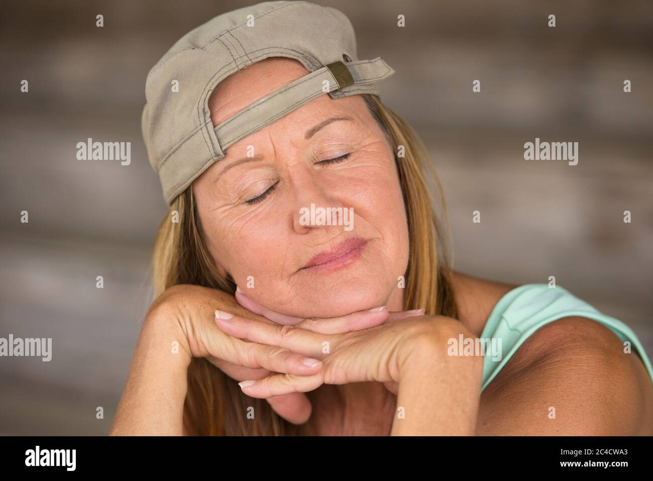 Portrait attractive fit active mature woman wearing green sporty top and cap, happy sleepy relaxed, chin resting on hands, closed eyes, blurred backgr Stock Photo