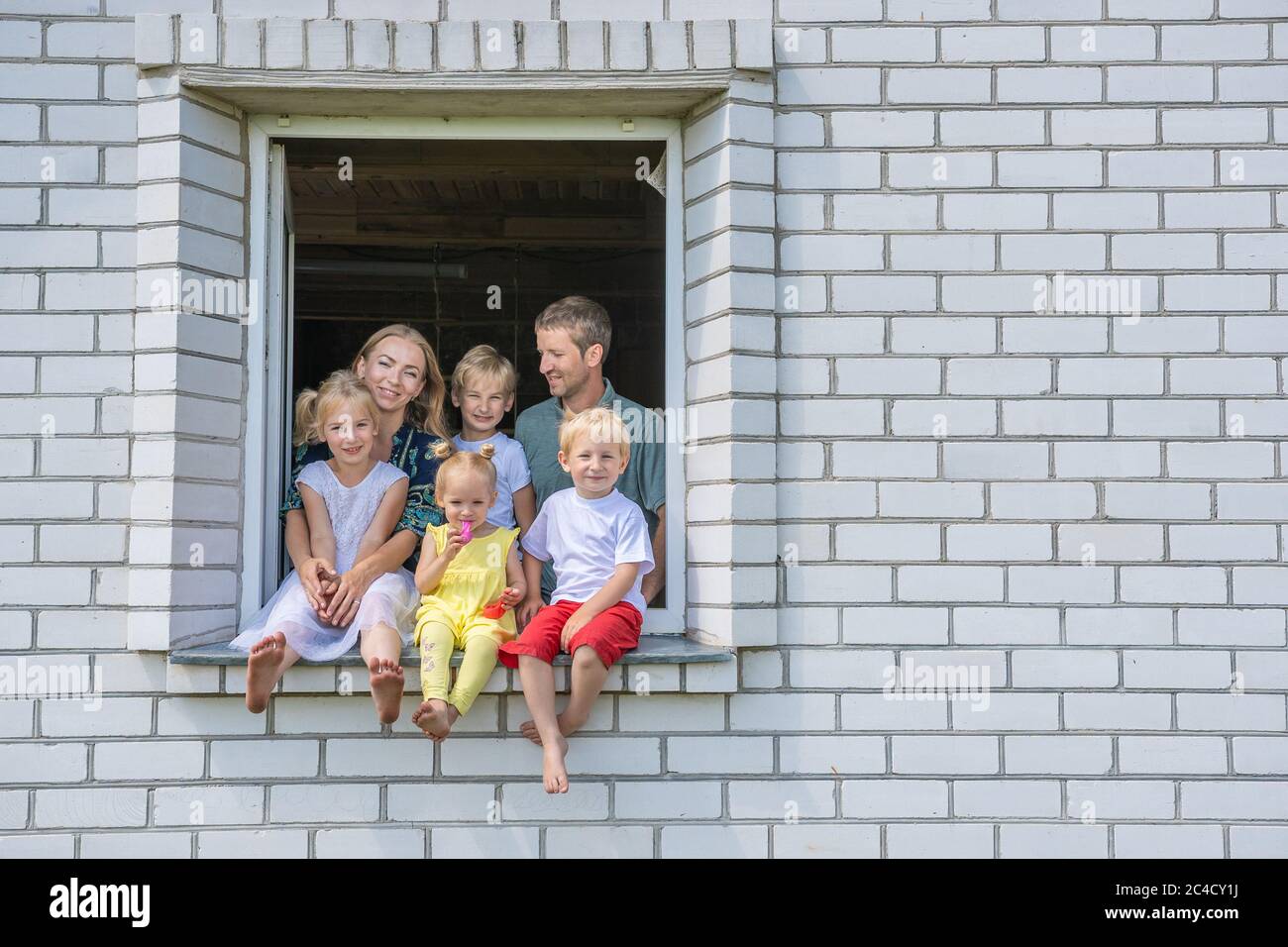 A large large family poses from the window of their home. Stock Photo