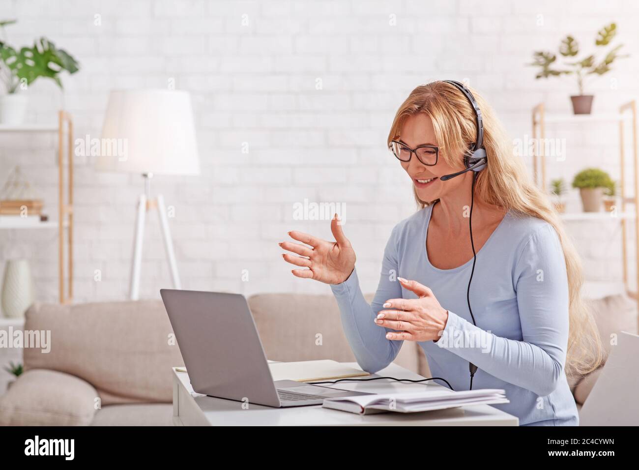 Support and online consultation from home. Woman with headset works remotely at laptop Stock Photo