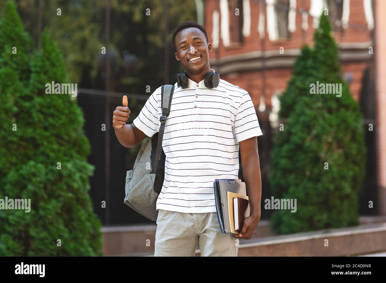 Happy black male student posing outdoors and showing thumb up gesture Stock Photo