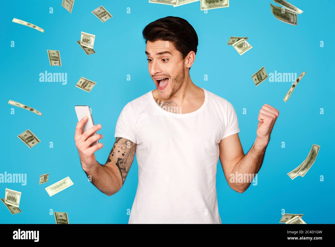 Lucky Winner. Excited Man With Smartphone Screaming With Joy Under Money Shower Stock Photo