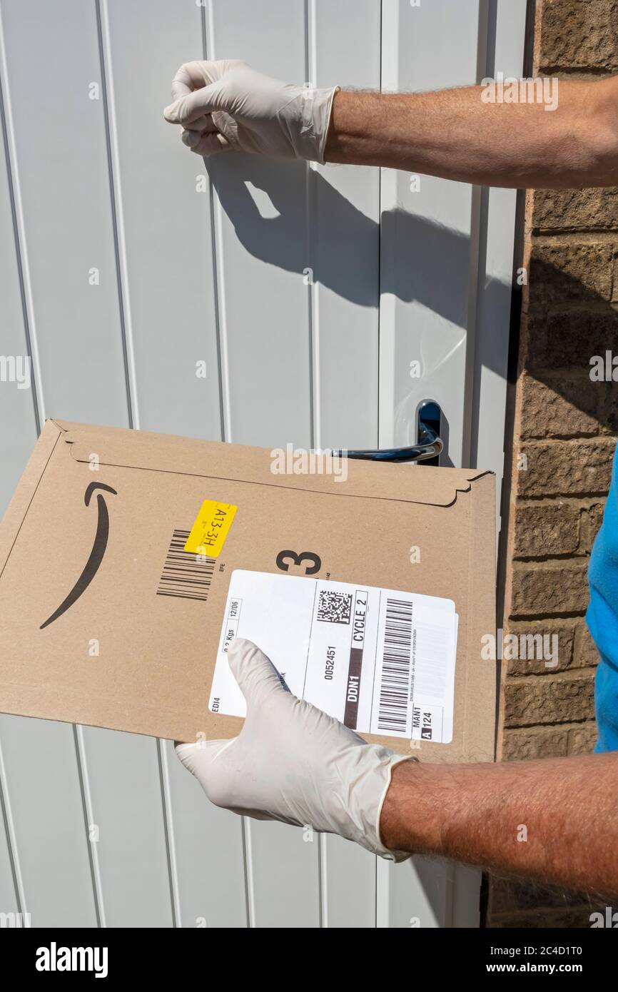 Man person knocking on house door wearing protective gloves covid 19 delivering holding Amazon delivery packet package England UK United Kingdom Stock Photo