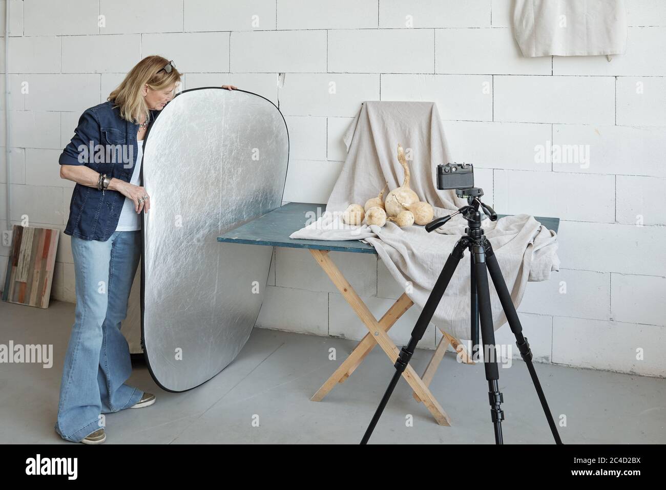 Mature photographer in denim outfit adjusting lighting reflector while