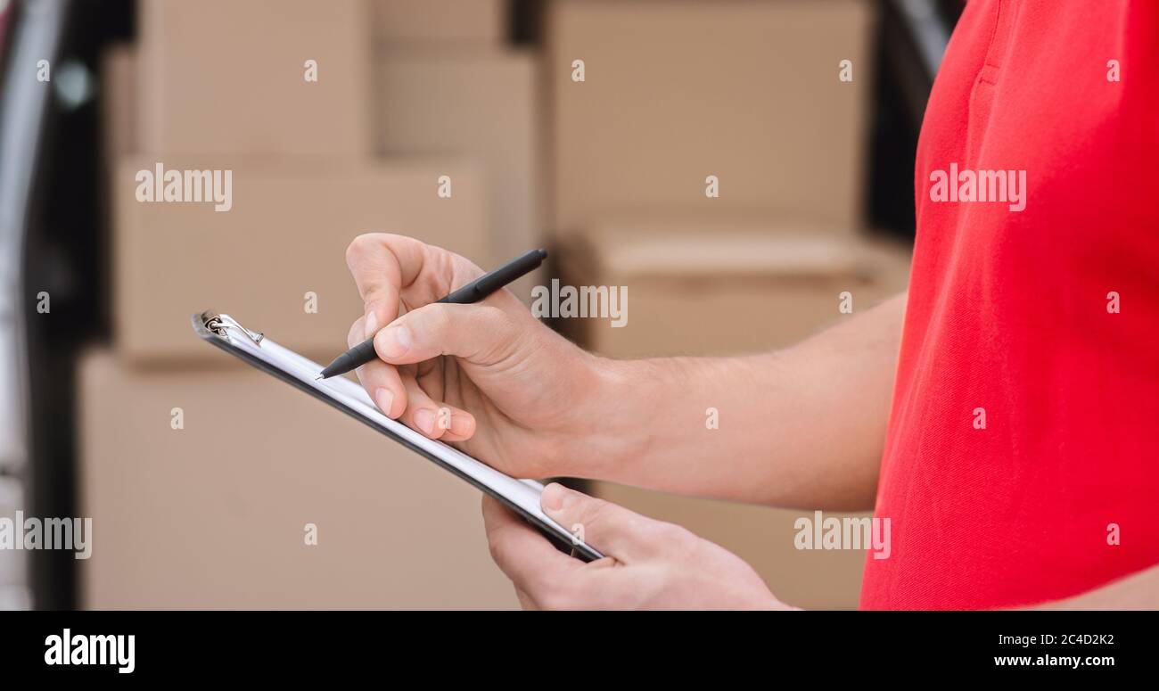 Accurate delivery. Courier notes to tablet delivered parcel, close up, a lot of boxes in car nearby Stock Photo