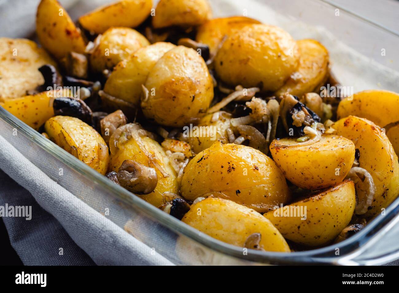 Roasted young potatoes in glass baking dish with mushrooms. Angle view, Stock Photo