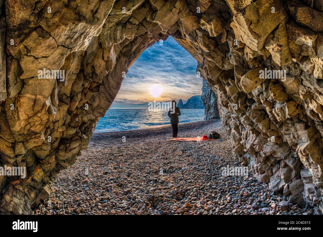 view from the stone cave on the sunset sea and the beach, the volcanic rock of the cave is lit by the warm setting sun. The concept of calmness Stock Photo