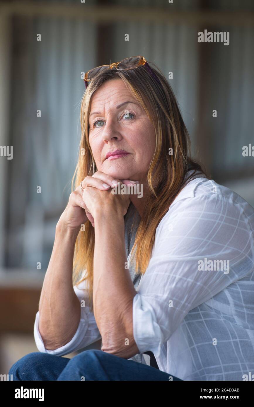 Portrait attractive mature woman sitting thoughtful relaxed and confident alone, daydreaming, smiling. Stock Photo