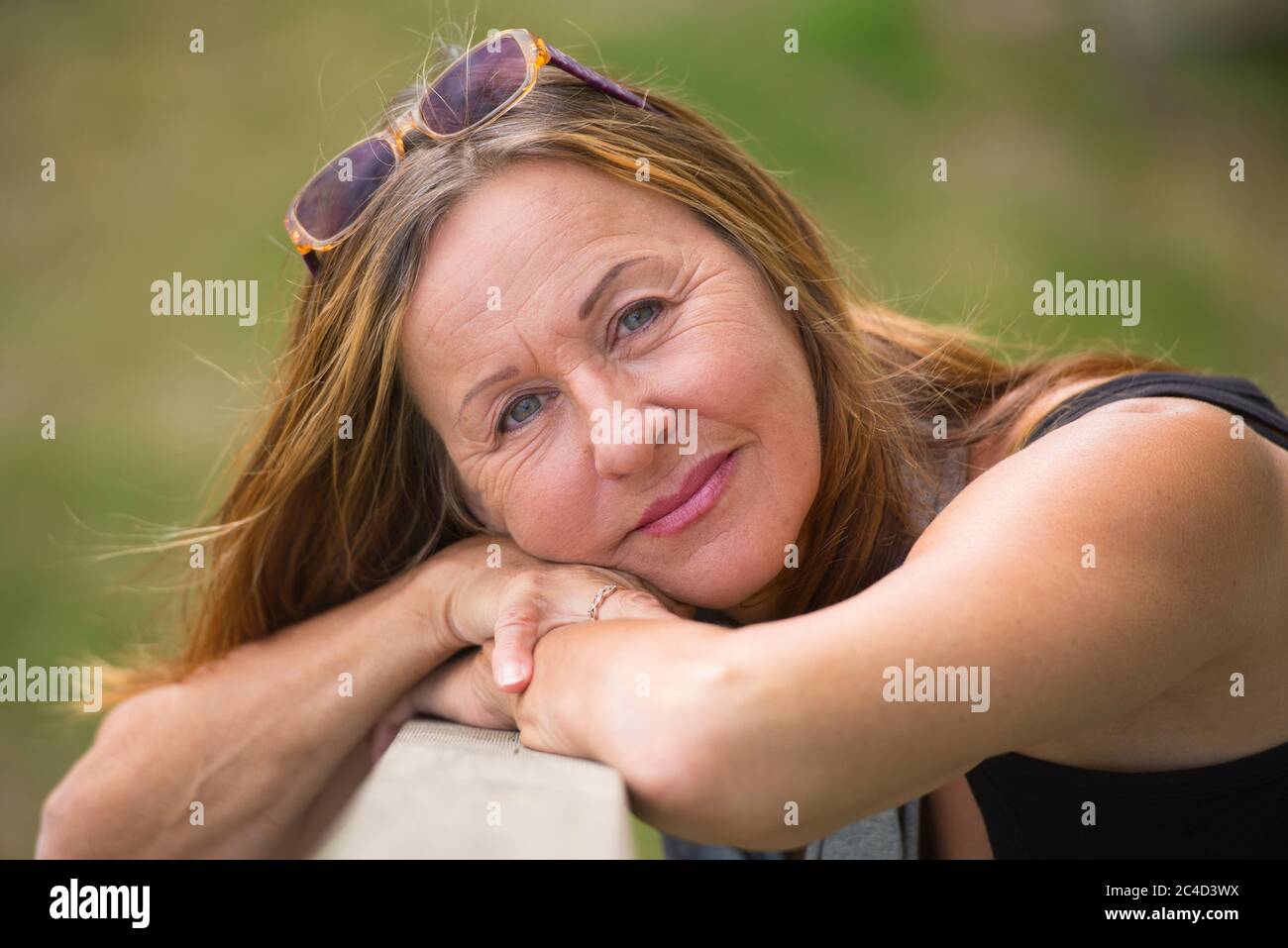 Portrait attractive mature woman relaxed and happy smiling outdoor with sunglasses, green blurred background and copy space. Stock Photo