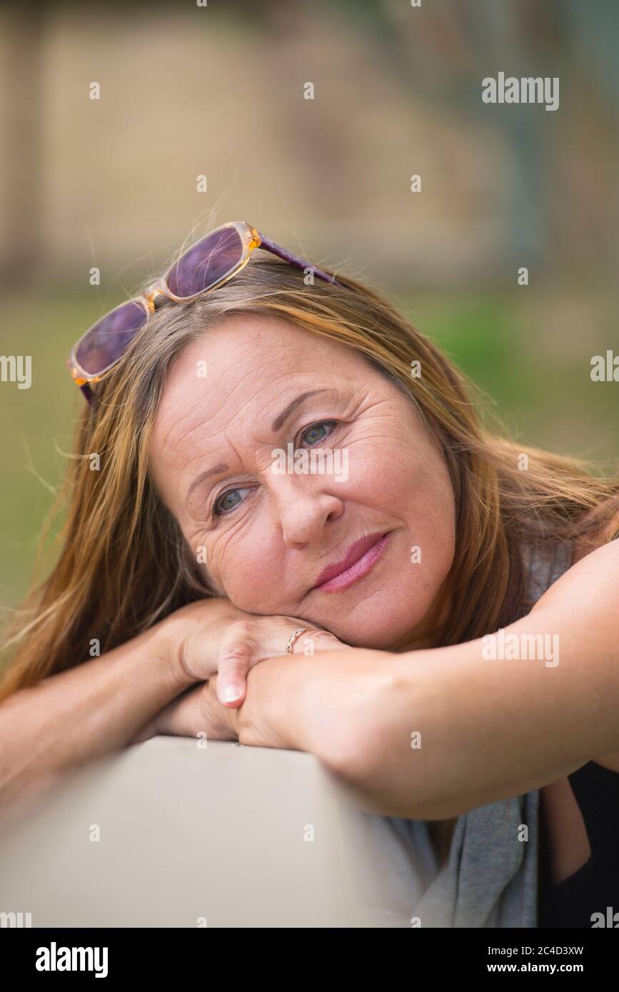 Portrait attractive mature woman posing relaxed laid back and happy smiling outdoor with sunglasses, green blurred background and copy space. Stock Photo