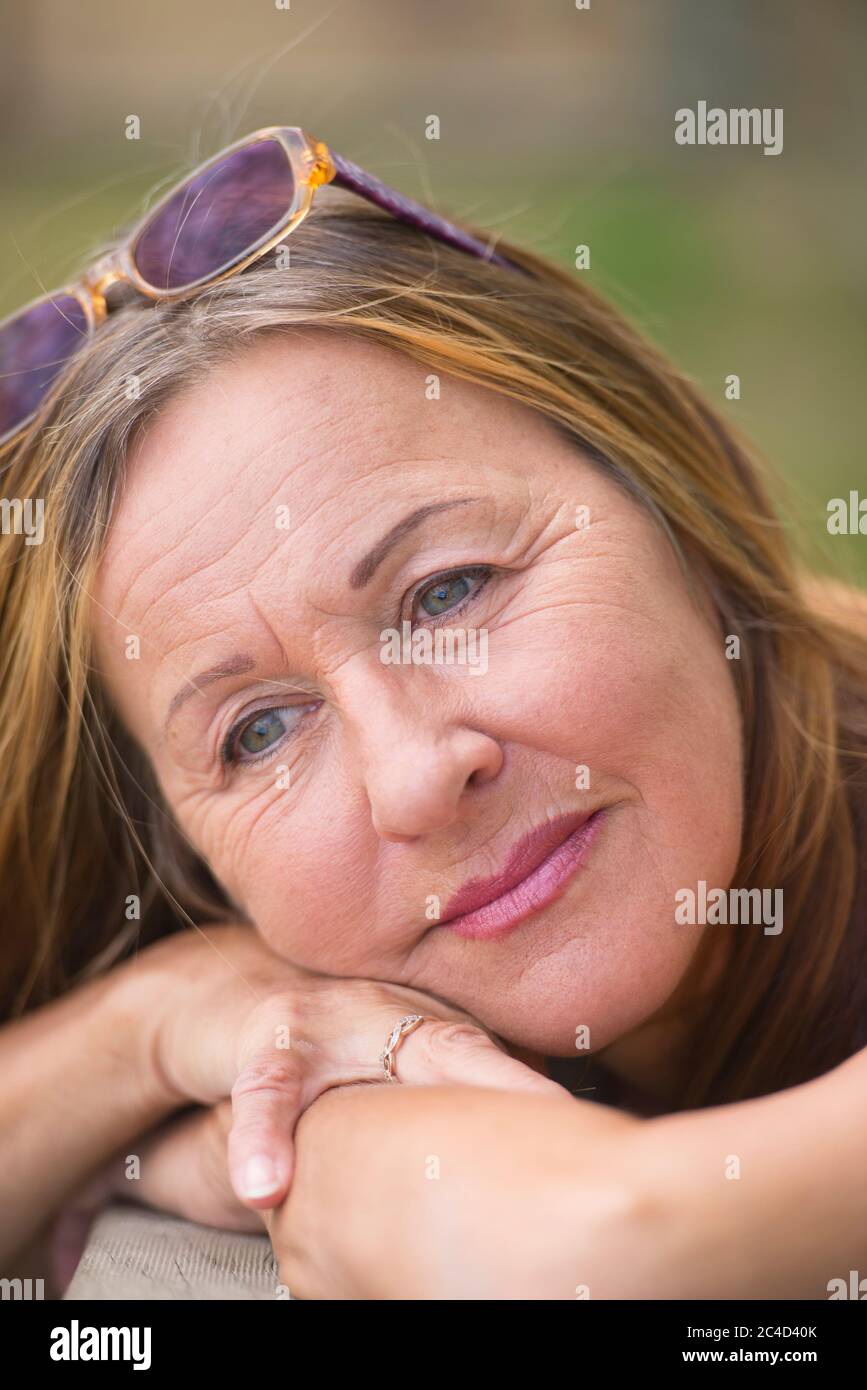 Portrait attractive mature woman posing relaxed and happy smiling outdoor with sunglasses, green blurred background and copy space. Stock Photo