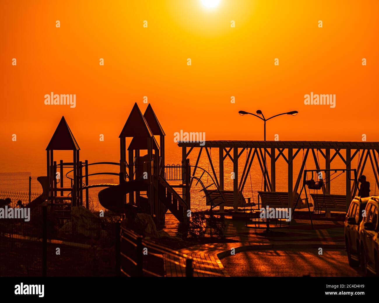 Red burning sunset over the sea with a silhouette of a playground and a ...