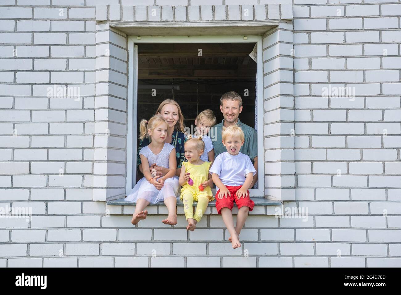 A large large family poses from the window of their home. Stock Photo