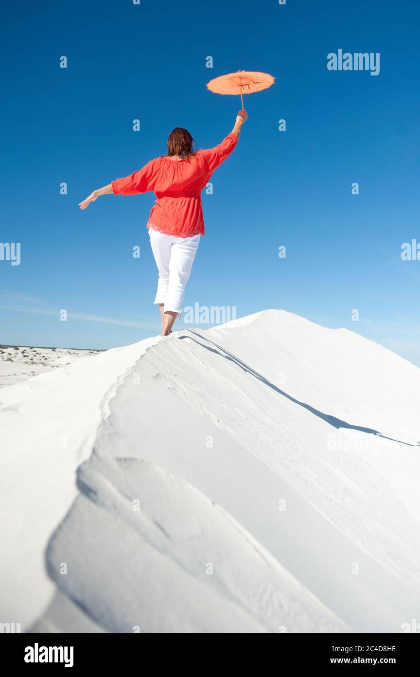 A mature woman is balancing on a sheer white sand dune in the desert ...