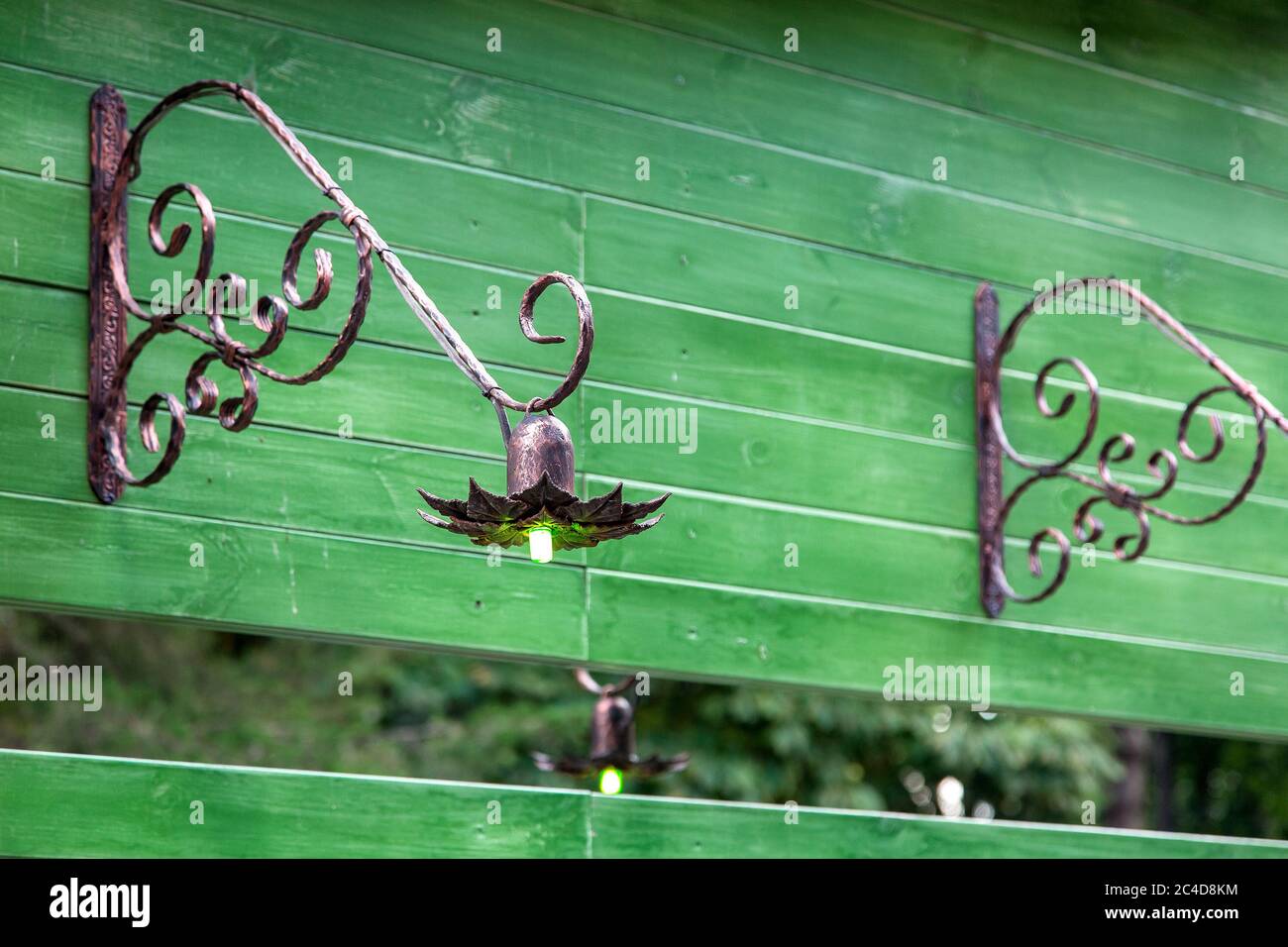 wall wrought iron street lamp with a luminous bulb on a green wooden