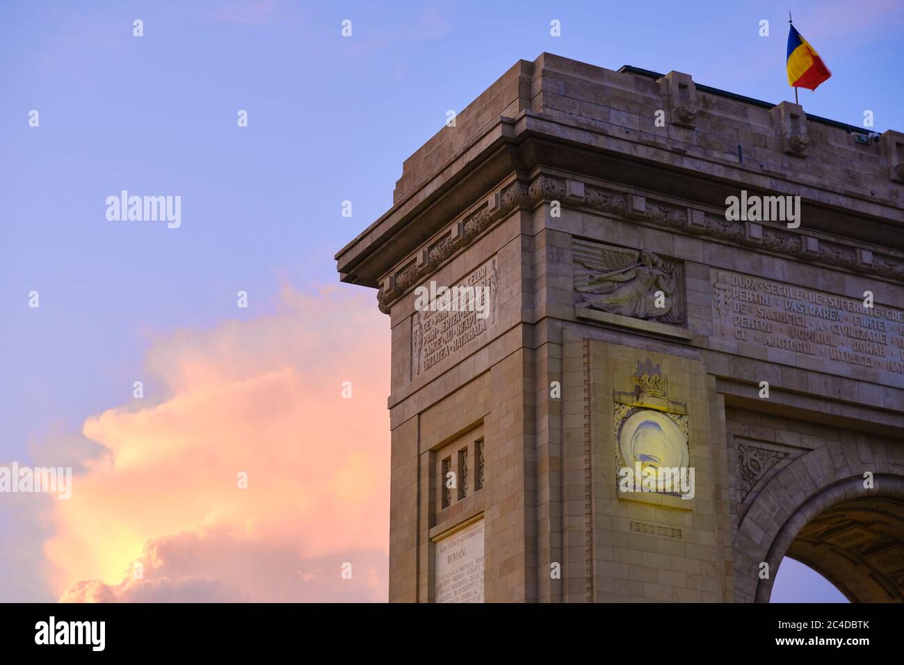 A corner of the Arch of Triumph in Bucharest, Romania, during a sunset with pink and orange clouds. Main touristic landmark, sightseeing spot. Stock Photo