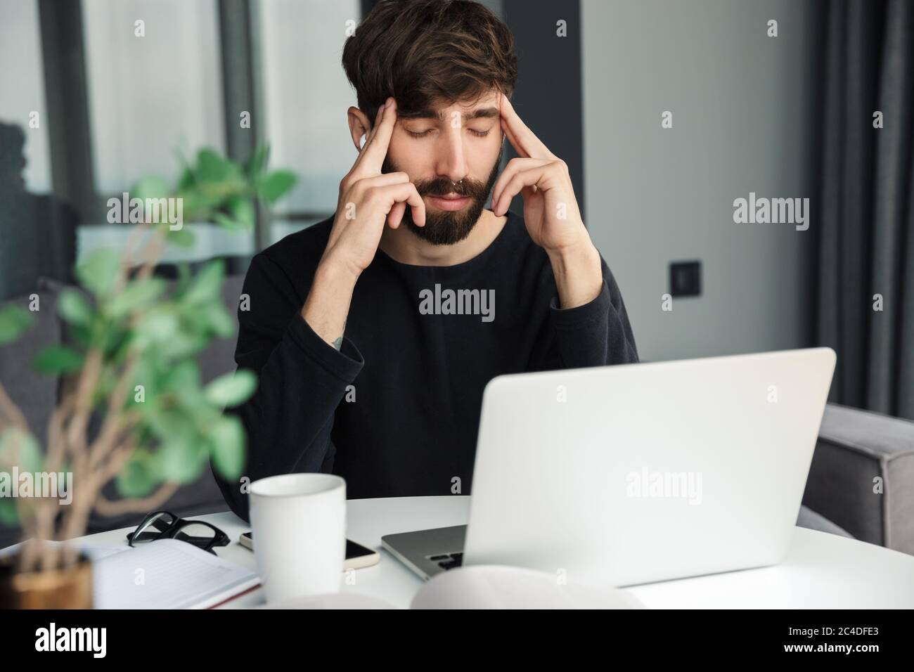 Image of tired man with headache using wireless earphones and laptop