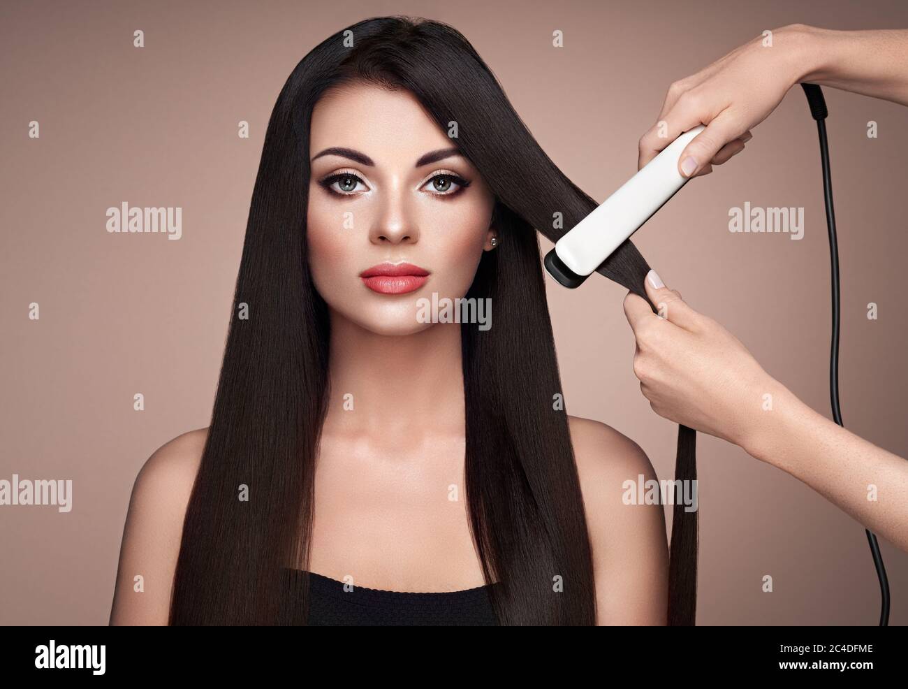 Hairdresser straightening long dark hair with hair irons. Beautiful woman with long straight hair. Smooth hairstyle Stock Photo