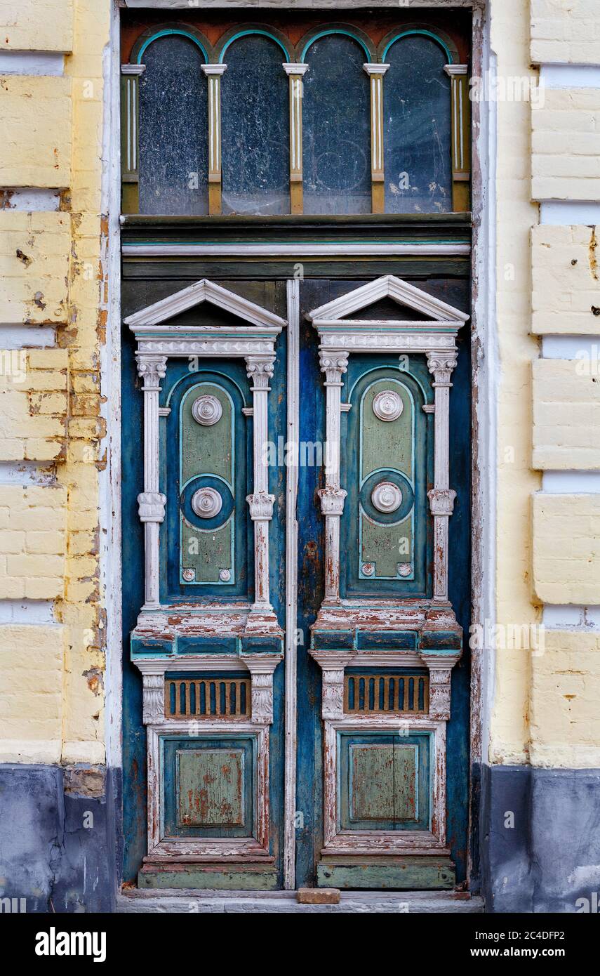 Old weathered wooden entrance doors with carved elements and a symmetrical pattern on the facade of an old house. Stock Photo