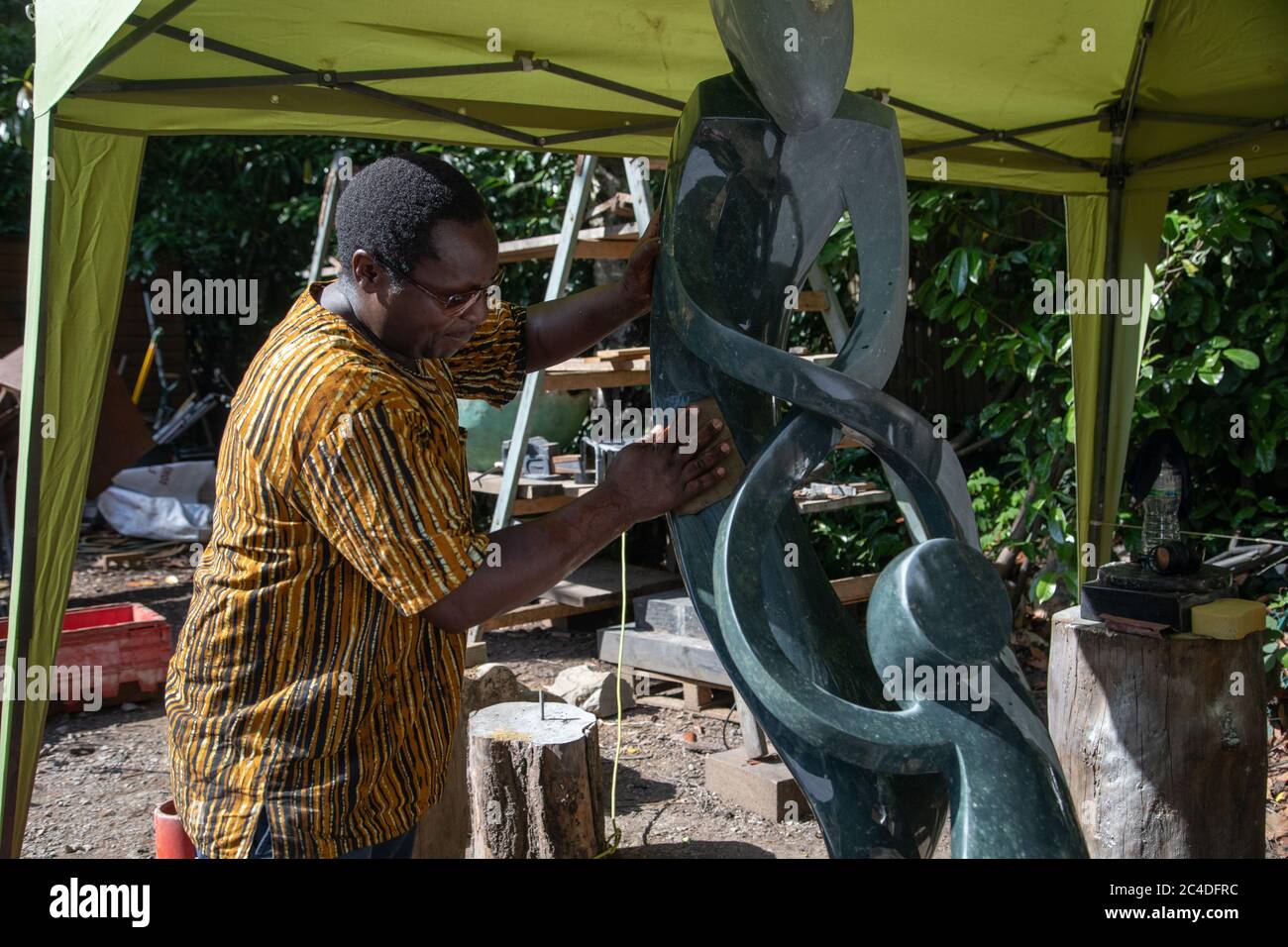 Churt, Surrey, UK. 26th June 2020. Zimbabwean sculptor Biggie Chikodzi working on a piece as Summers Place Auctions launches an online auction of Zimbabwean sculpture. Zimbabwe is the only country in Africa where artists make sculptures out of local stones. It is the first auction of its kind in the UK exclusively focusing on this African country’s artistic output.   Prices range from £200 to £40,000. The auction ends 5th July and includes works from famous first generation sculptors to younger third generation artists. Credit: Andy Sillett/Alamy Live News Stock Photo