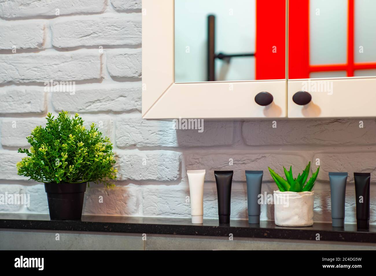 Close-up of shelf with decorative flower, cosmetics and hygiene gels. Loft interior of bathroom. Brick wall. Cabinet with mirror. Stock Photo