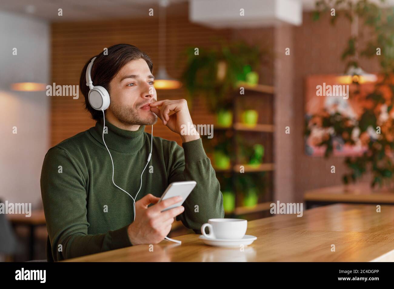 Pensive guy in headphones listening to music, using smartphone Stock Photo