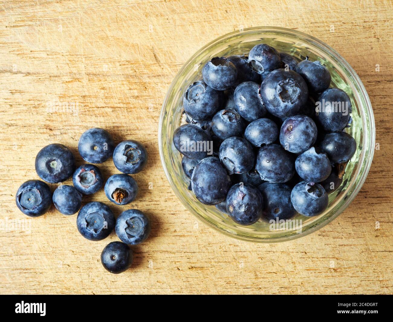 Fresh blueberries in a glass ramekin dish on a wooden chopping board with a handful of loose blueberries Stock Photo