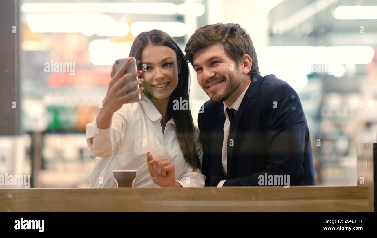 Happy young formaly dressed couple using cell phones and taking Stock Photo