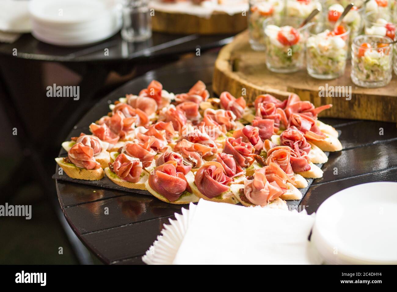 Many sandwiches with jamon and sauce on dark wooden table. Lot of bruschettas with ham or parma. Snack baguette with meat. Catering food concept Stock Photo