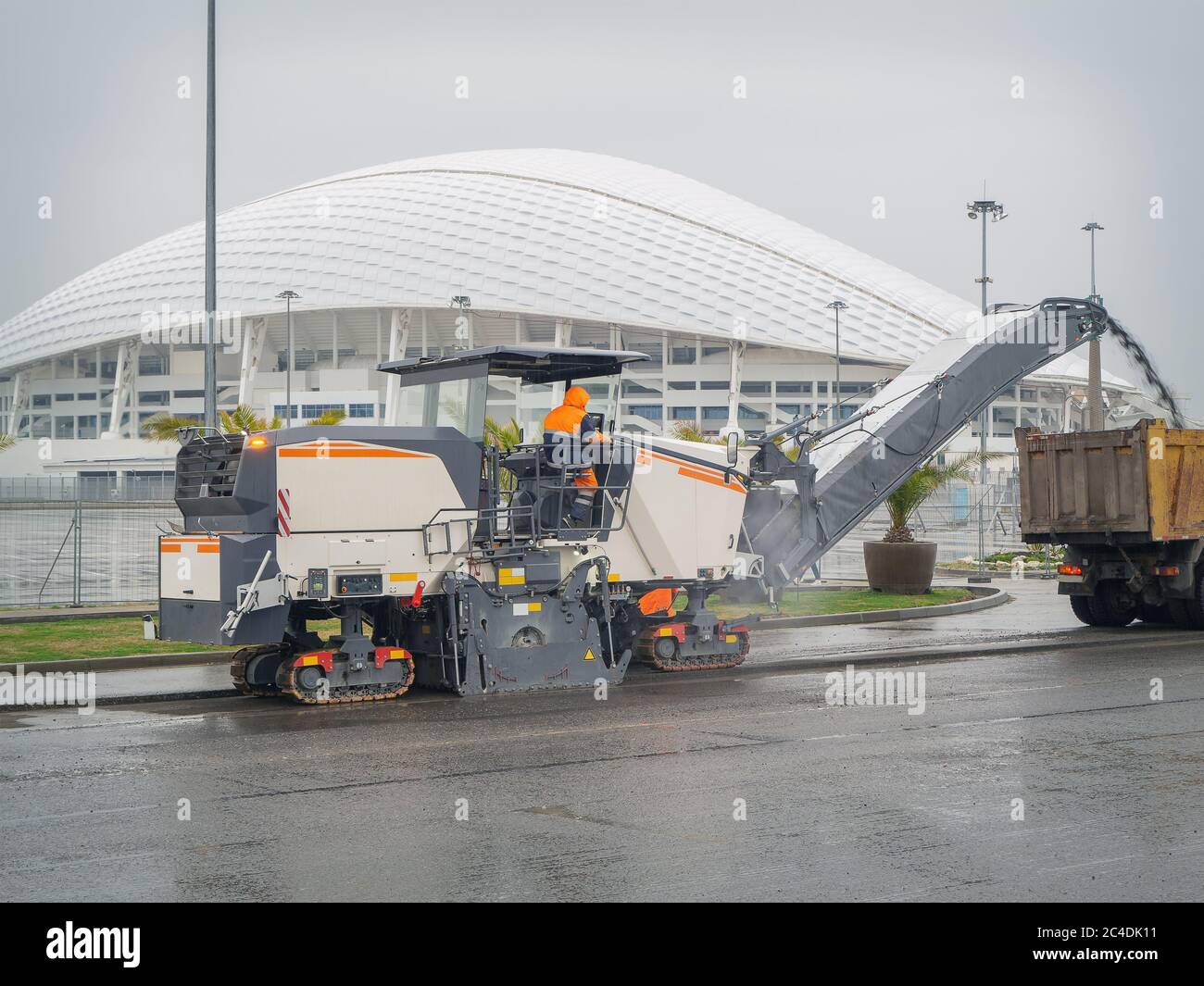 A road mill loads crushed asphalt into a dump truck on the background of a domed white building. Men at work Stock Photo