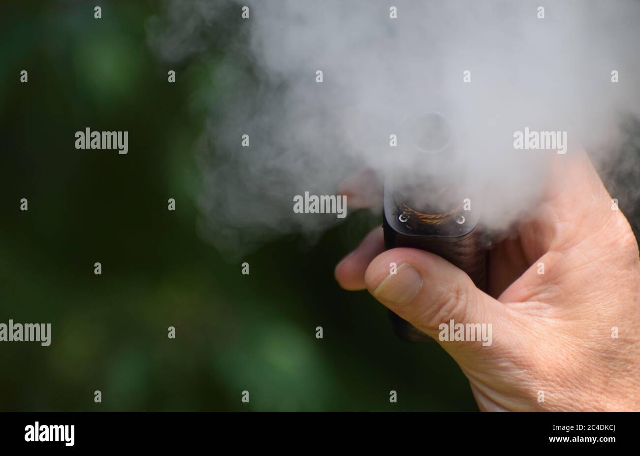 A close up of a man's hand holding an e-cigarette / vaping mod as he vapes creating lots of vape mist Stock Photo