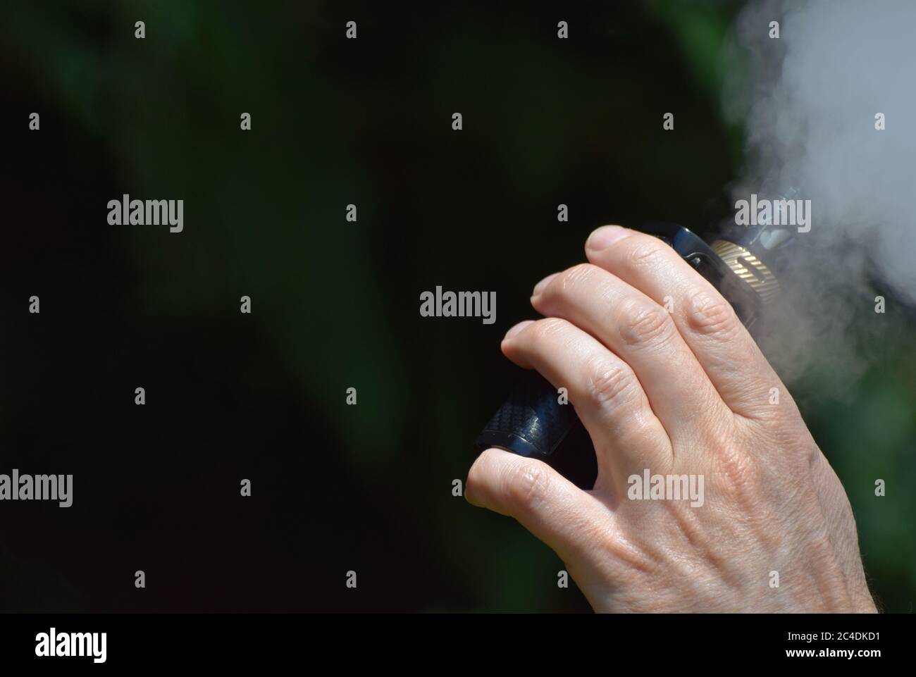 A close up of a man's hand holding an e-cigarette / vaping mod as he vapes creating lots of vape mist Stock Photo