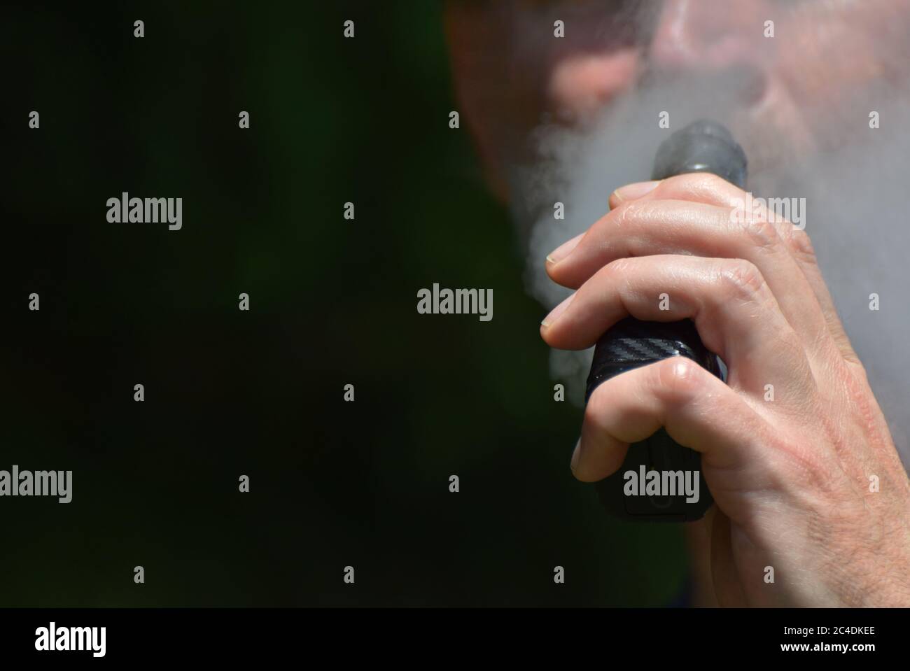 A man vaping with focus on his hand as he holds the e cigarette / vape mod up to his mouth while exhaling vapour Stock Photo
