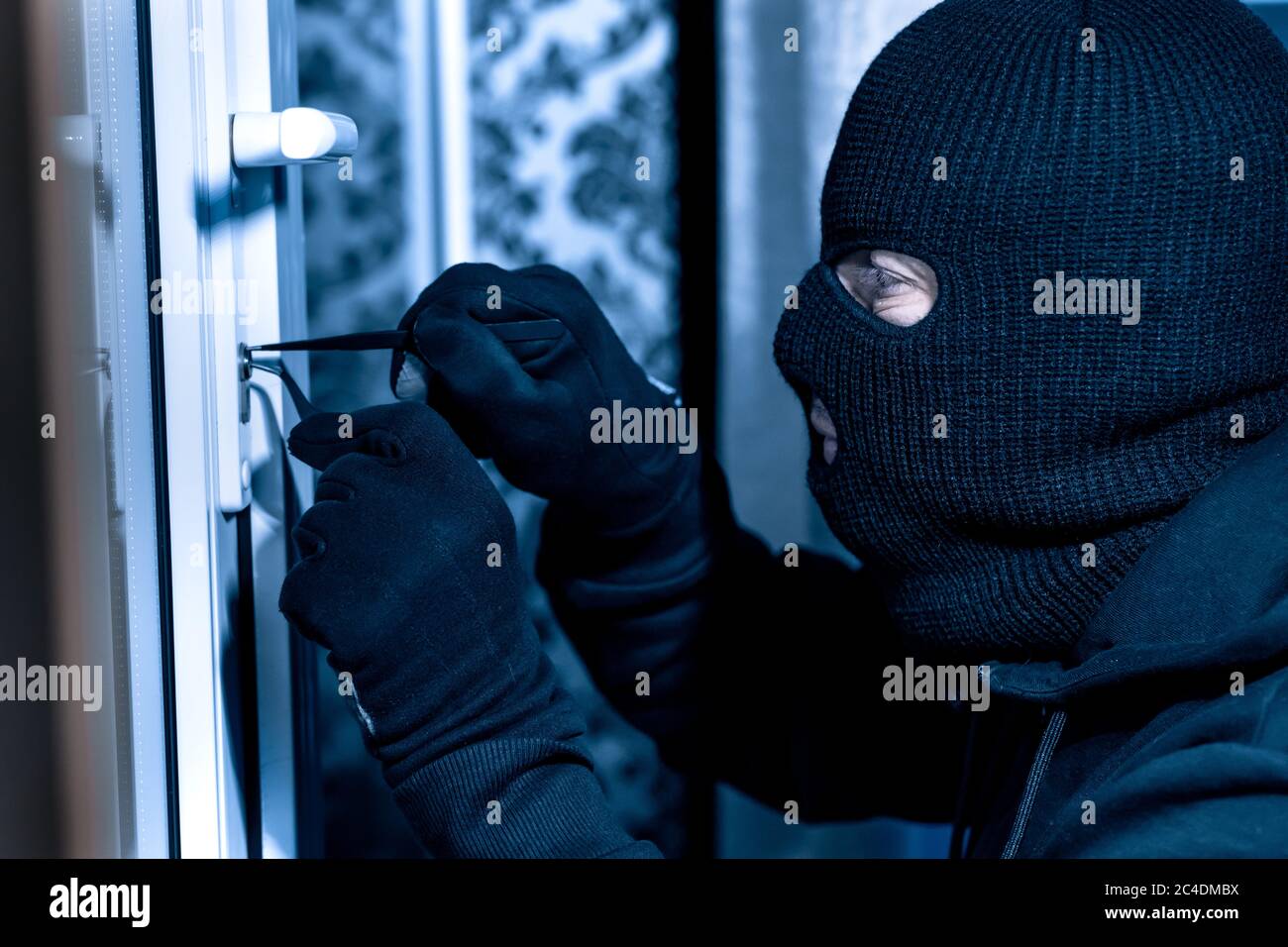 Robber in black balaclava cracking door with metal picklock Stock Photo