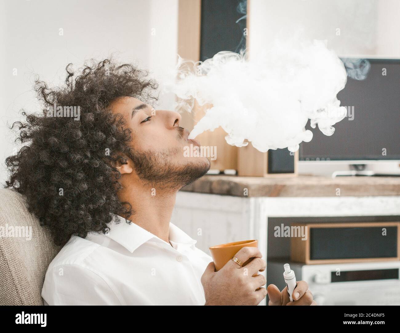 Profile view of shaggy man smoking of e-cigarette and drinking coffee. Copy space in white smoke cloud. Close up shot. Tinted image Stock Photo