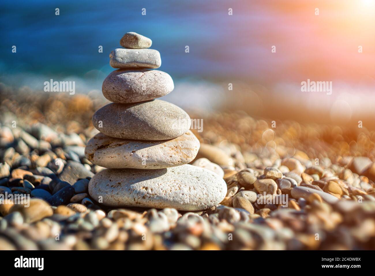 Balanced Pebbles Pyramid on the Beach on Sunny Day and Clear Sky at Sunset. Blue Sea on Background Selective focus, zen stones on sea beach Stock Photo