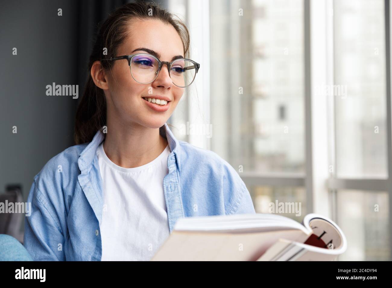 Image of cheerful caucasian cute woman in eyeglasses reading book and ...